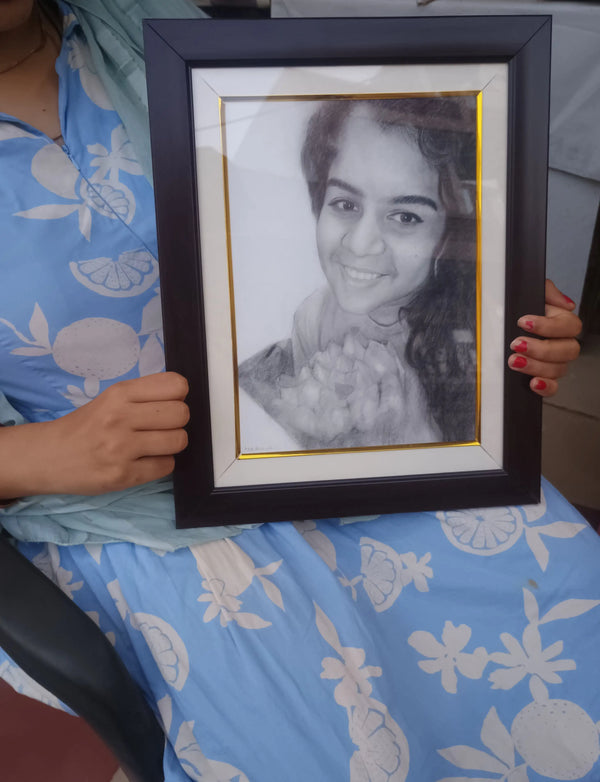 A person in a blue floral dress holds a black picture frame with a white mat and a gold inner border, containing a black and white portrait of a smiling woman.