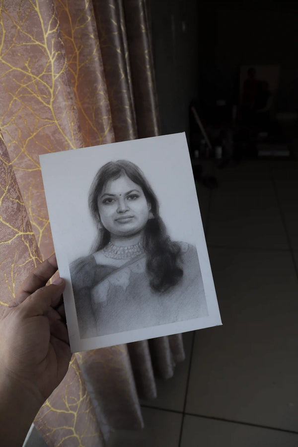 A hand holds a black and white pencil sketch portrait of a woman in front of a patterned curtain in a dimly lit room.