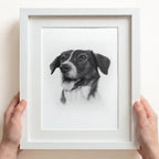 Custom dog pencil sketch portrait in a white frame with white mount board, held by hands on a light background.