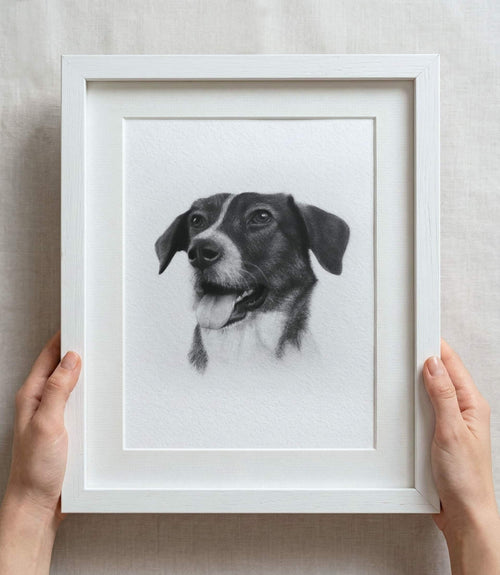 Custom dog pencil sketch portrait in a white frame with white mount board, held by hands on a light background.