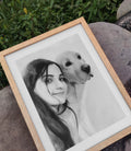 A framed pencil drawing of a woman with a beagle dog, displayed on a wooden easel with a natural background.