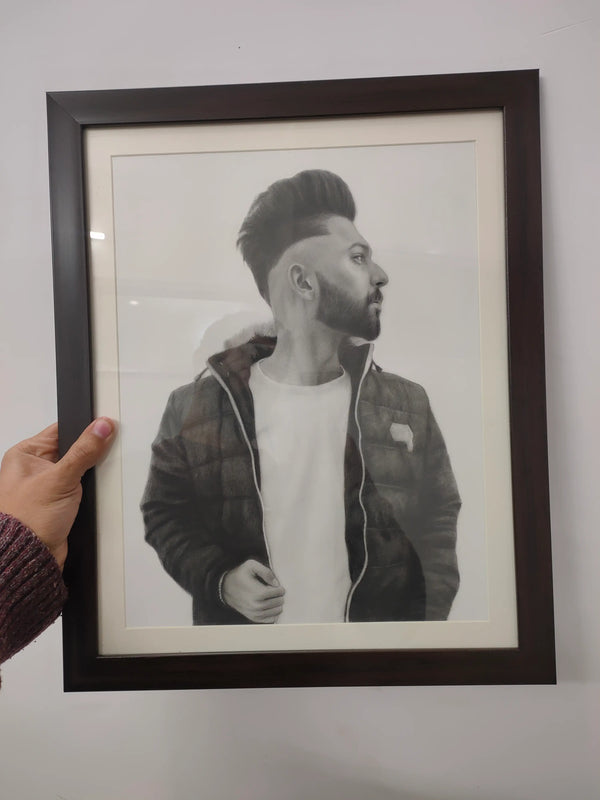 A framed black and white portrait print of a man, held by a hand on the left against a plain light gray wall.