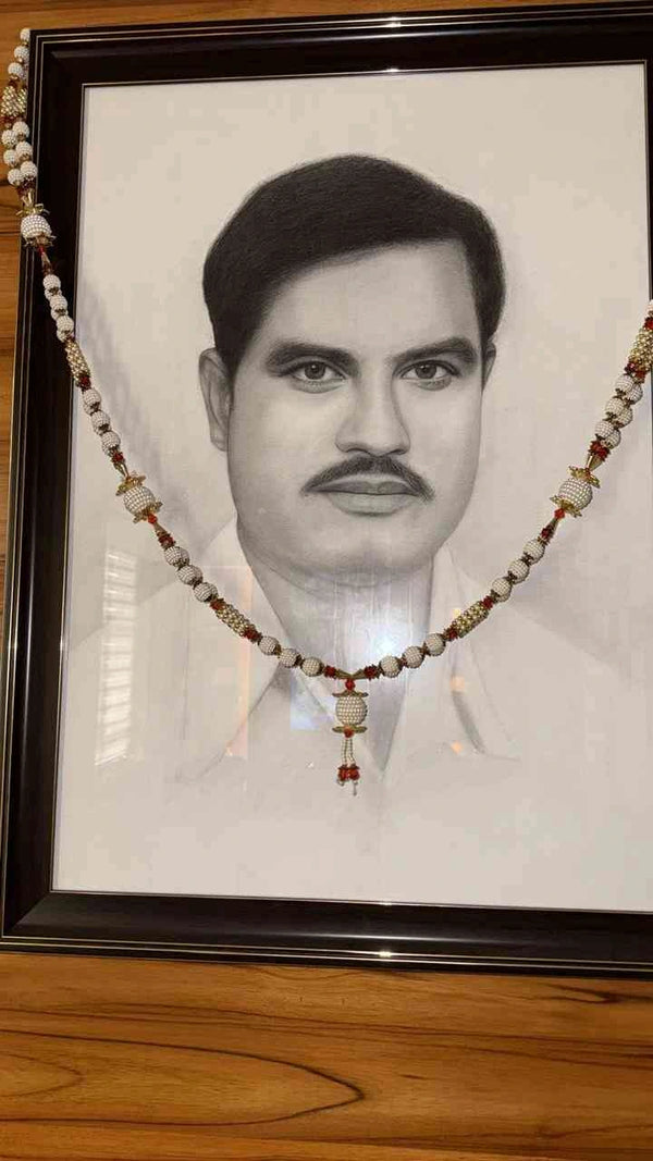 A framed black and white portrait print of a man, decorated with a beaded garland draped across the picture, resting on a wooden surface.